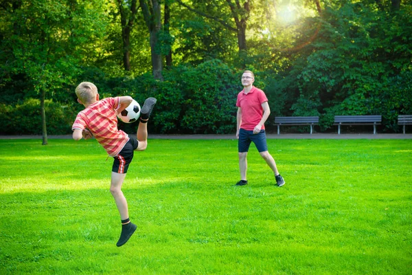幸せな若いです父遊びとともに彼の小さな息子サッカーで緑の日当たりの良い公園 — ストック写真
