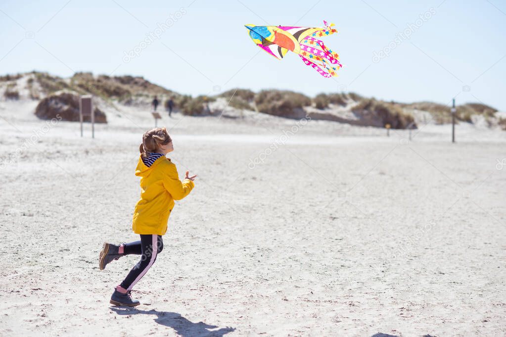 Cheerful little girl running in dress on beach with kite at sunny day