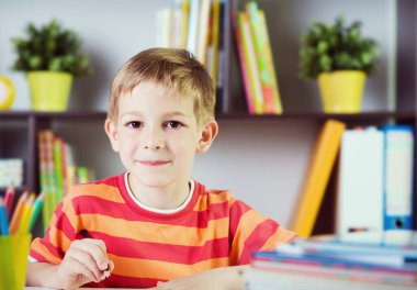 İlkokul çocuğu sınıf masasında ödev yapıyor.