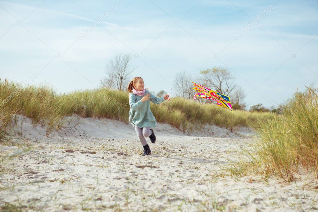 Cheerful little girl running in dress on beach with kite at sunny day