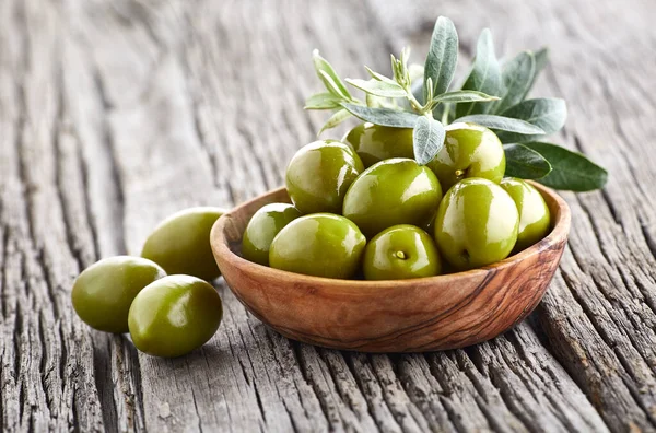 Green greek olives with leaves on wooden background