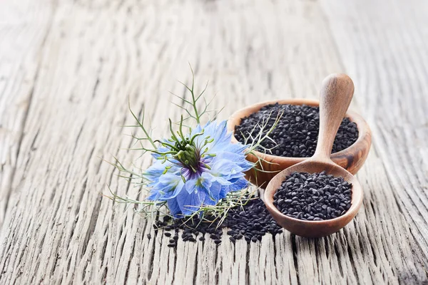 Black cumin seeds with flower on wooden board