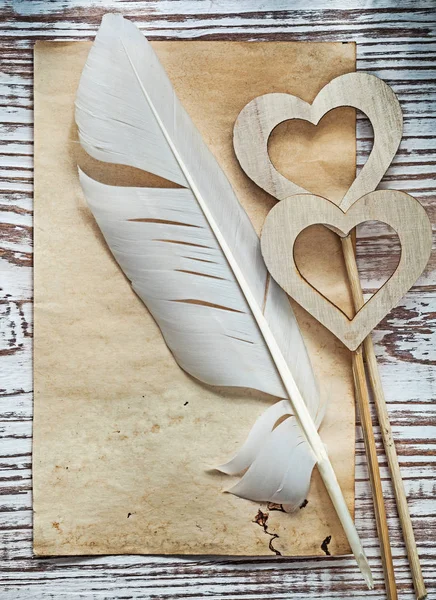 Old paper sheet plume wooden hearts on vintage wood board holida