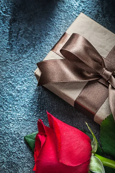 Present box with brown bow red rose on black background holidays