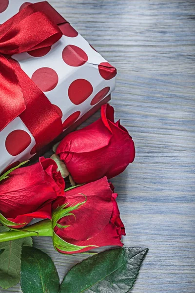 Present box with knot expanded red roses on wooden board holiday — Stock Photo, Image