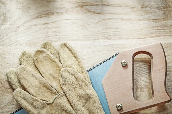 Sepasang sarung tangan pelindung kulit gergaji besi tajam di papan kayu — Stok Foto