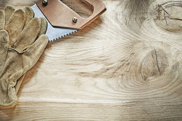 Par de guantes protectores sierra de mano afilada en tablero de madera construc —  Fotos de Stock