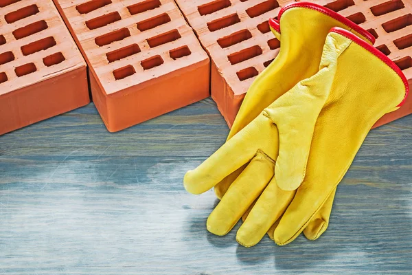 Briques de construction gants de protection jaunes sur panneau en bois brique — Photo