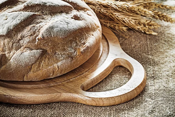 Chopping board bread wheat ears on vintage hessian background — Stock Photo, Image