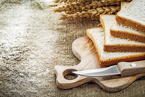 Wooden chopping board knife sliced bread wheat ears on hessian b