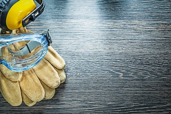 Set of leather protective gloves goggles earmuffs on wooden boar — Stock Photo, Image