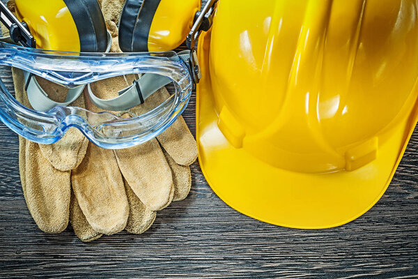 Safety gloves goggles earmuffs hard hat on wooden board