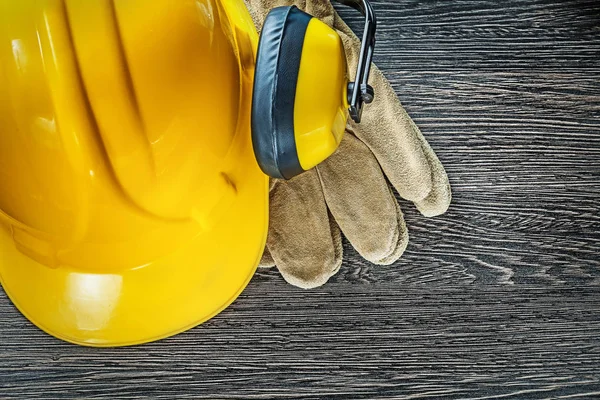 Hard hat earmuffs leather safety gloves on wooden board — Stock Photo, Image