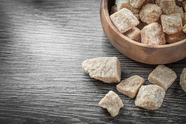 Cubos de açúcar marrom na tigela na tábua de madeira vintage — Fotografia de Stock