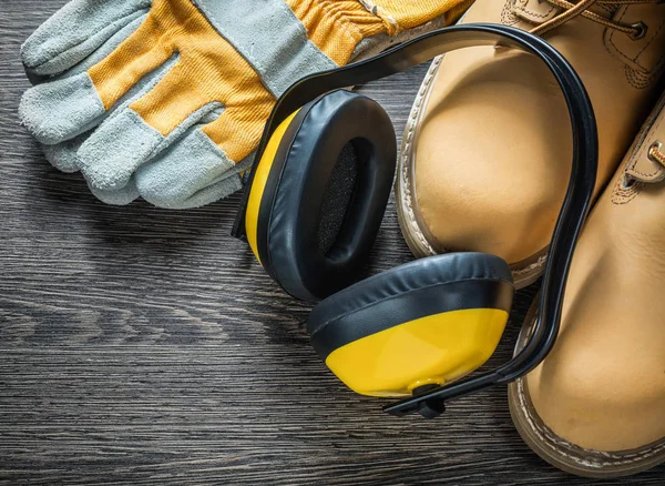 Schutzhandschuhe wasserdichte Arbeitsstiefel Ohrenschützer auf Holzbrett — Stockfoto