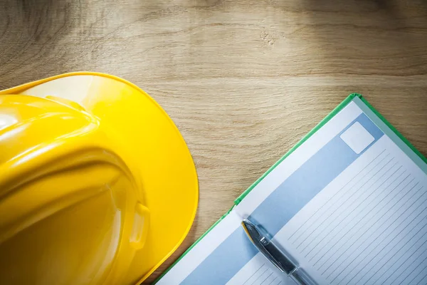 Opened notepad ballpoint pen safety hard hat on wooden board — Stock Photo, Image