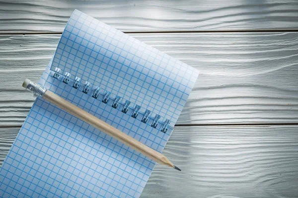 Lápis de bloco de notas em espiral em branco verificado na placa de madeira branca — Fotografia de Stock