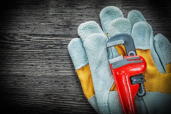 Chiave per tubi idraulici guanti protettivi su tavola di legno — Foto Stock