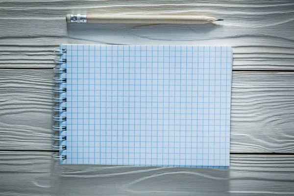 Checked spiral notepad pencil on white wooden board