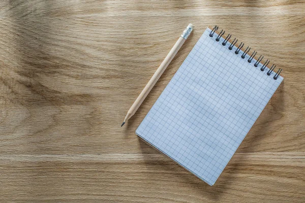 Checked spiral notepad pencil on wooden board directly above — Stock Photo, Image