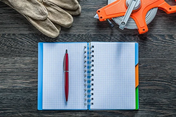 Measuring tape safety gloves notebook pen on wooden board — Stock Photo, Image