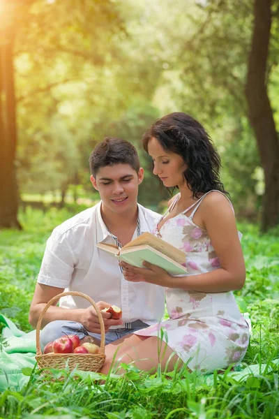 Joven pareja enamorada en verde parque leer un libro y comer un —  Fotos de Stock