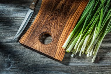 Mutfak bıçağı ahşap doğrama tahtası taze bahar yeşil soğanı eski ahşap arka planda saplanır
