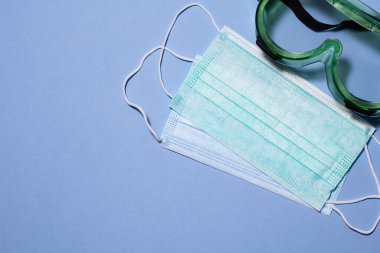 Tıbbi maskeler ve mavi arka planda doktorun özel gözlükleri. Boşluğu kopyala