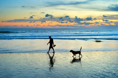 Silhouette of a man and dog walking on a beach at sunset. Bali island, Indonesia clipart