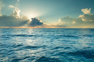 Bulutlar mavi gökyüzünde sakin denizin üzerinde güneş ışığı yansımasıyla