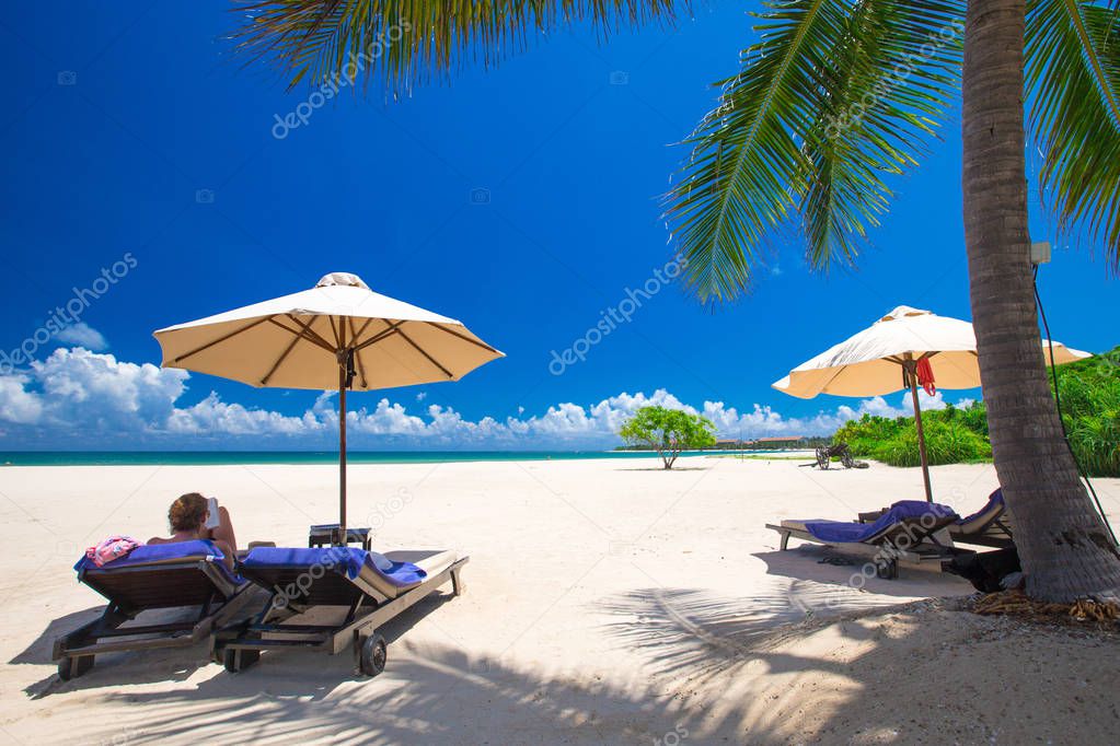 Palm trees on white sandy beach with deck chairs and umbrellas