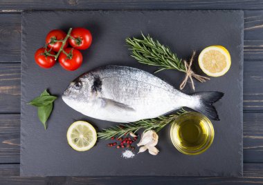 Dorado çiğ balık pişirme ve malzemeler. Dorado, limon, domates, otlar ve baharatlar. Ahşap tabl üzerinde Üstten Görünüm