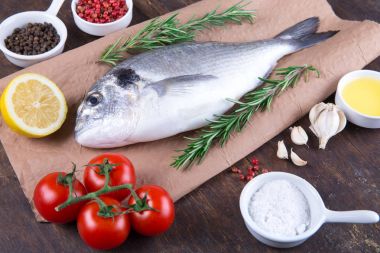 Dorado çiğ balık pişirme ve malzemeler. Dorado, limon, domates, otlar ve baharatlar. Ahşap tabl üzerinde Üstten Görünüm