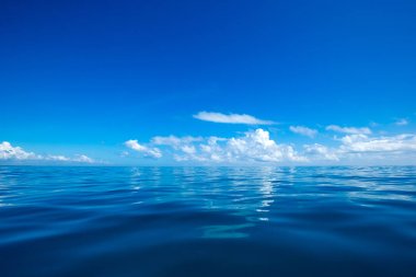 Bulutlar mavi gökyüzünde sakin denizin üzerinde güneş ışığı yansımasıyla