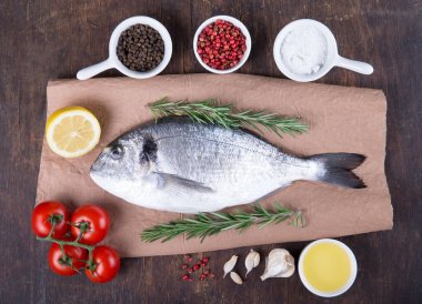 Dorado çiğ balık pişirme ve malzemeler. Dorado, limon, domates, otlar ve baharatlar. Ahşap masa üzerinde Üstten Görünüm
