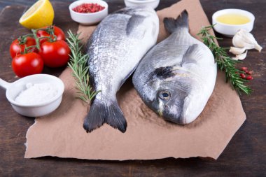 Dorado çiğ balık pişirme ve malzemeler. Dorado, limon, domates, otlar ve baharatlar. Ahşap masa üzerinde Üstten Görünüm