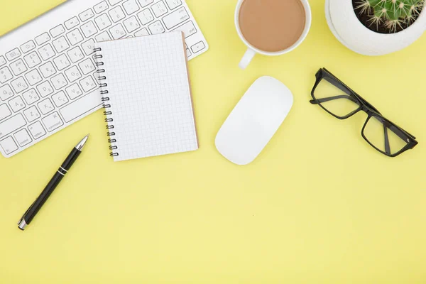 workspace with tablet, keyboard, coffee cup and eyeglasses copy space on yelow background. Top view.