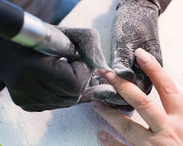 Befälhavaren använder en elektrisk maskin att ta bort nagellack på händerna under manikyr i salongen. Hårdvara manikyr. Begreppet kroppsvård Stockfoto