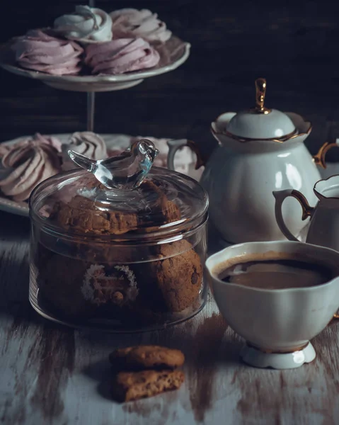 Стеклянная банка с печеньем и чашка на деревянном столе на темном фоне. Винтажный стиль — стоковое фото