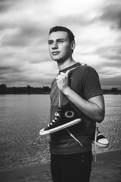 Young man standing on the river bank with trainers — Stock Photo, Image