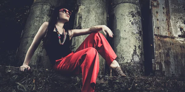 빨간 바지와 안경 산업 배경 위에 앉아 있는 여자 — 스톡 사진