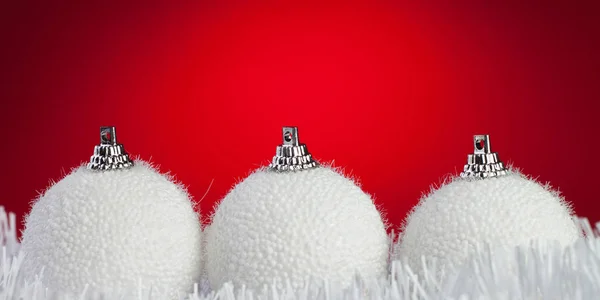 Three white christmas balls on tinsel over bright red background — Zdjęcie stockowe
