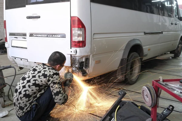 Worker works with angle grinder in a car repair shop — Stock Photo, Image