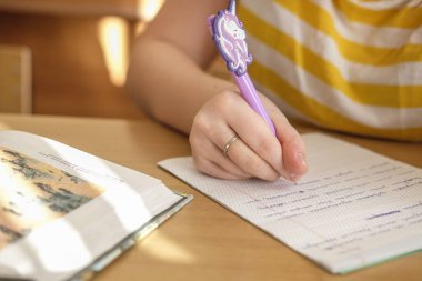 Okulda bir not defterine yazan bir öğrencinin el resmi.