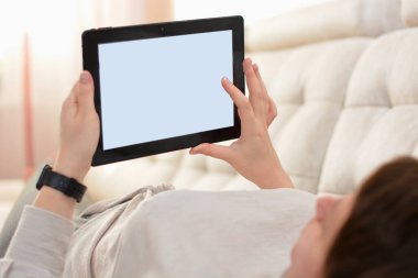 Tabletli kadın kanepeye uzanmış, arka planı parlak. Yumuşak odak.