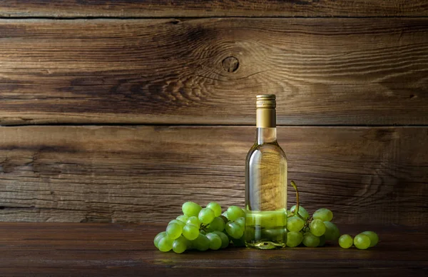 Uma garrafa de vinho branco com uvas em um fundo de madeira — Fotografia de Stock