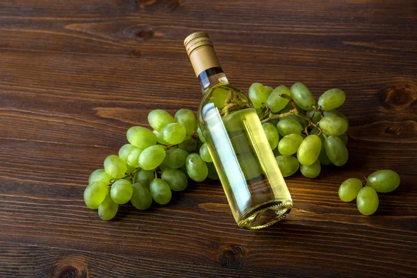 Een fles witte wijn met druiven op een houten achtergrond — Stockfoto