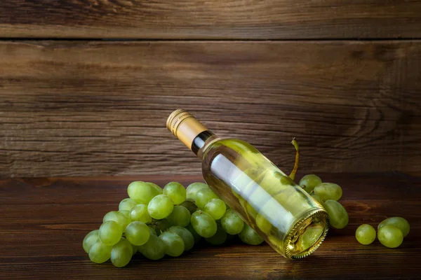 Een fles witte wijn met druiven op een houten achtergrond — Stockfoto