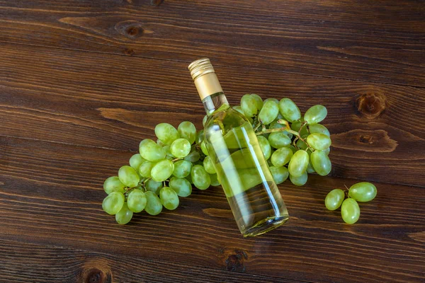 Een fles witte wijn met druiven op een houten achtergrond — Stockfoto