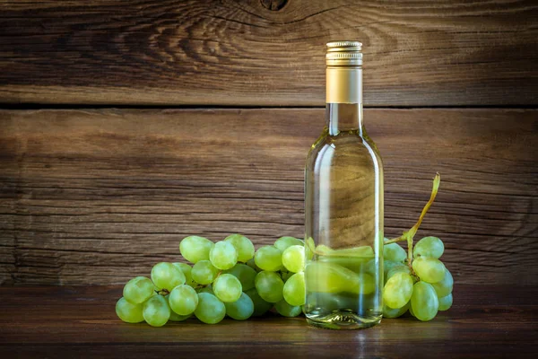 Uma garrafa de vinho branco com uvas em um fundo de madeira — Fotografia de Stock